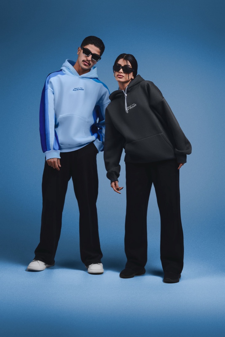 Two models in oversized hoodies against a blue studio backdrop